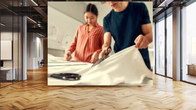 Out of the best materials. Cropped shot of young male designer cutting white fabric textile in a studio. Group of creative millennials working together Wall mural