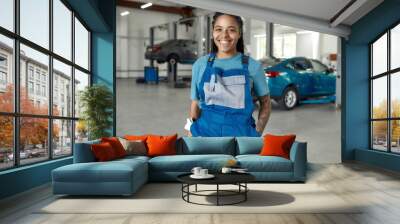 Perfect service. Portrait of young african american woman, professional female mechanic in uniform smiling at camera, standing in auto repair shop. Car service, repair, maintenance and people concept Wall mural