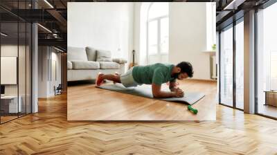 Perseverance matters. Young active man looking focused, exercising, doing plank during morning workout at home. Sport, healthy lifestyle Wall mural