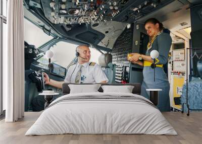 Pleased airline captain being served a drink in the cockpit Wall mural