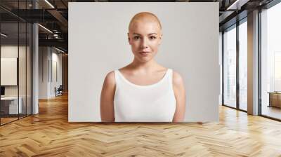 Portrait of a beautiful young caucasian woman with shaved head wearing white shirt, looking at camera while posing isolated over grey background Wall mural