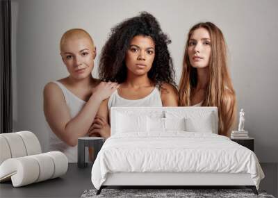 Portrait of three young diverse women wearing white shirts looking at camera while posing together isolated over grey background Wall mural