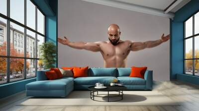 Showing his perfect body. Muscular strong bald man with naked torso standing with outstretched arms isolated over grey background Wall mural