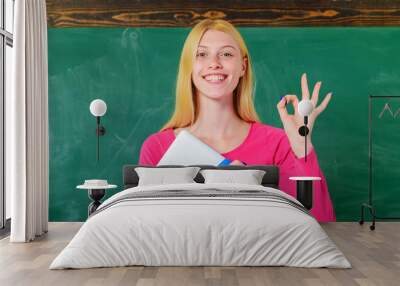 Smiling student in classroom showing okay. Female teacher with notebook make ok sign with fingers. Wall mural