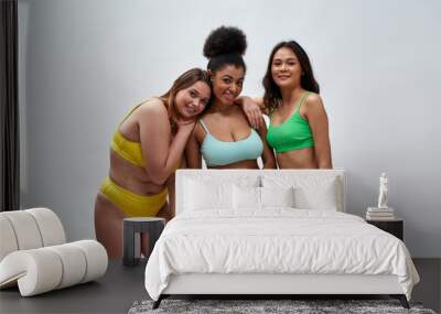 Three happy young women with different body shapes wearing colorful underwear smiling at camera while posing together isolated over light background Wall mural