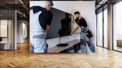 Two professional technicians, workers in uniform installing television on the wall indoors. Construction, maintenance and delivery concept Wall mural