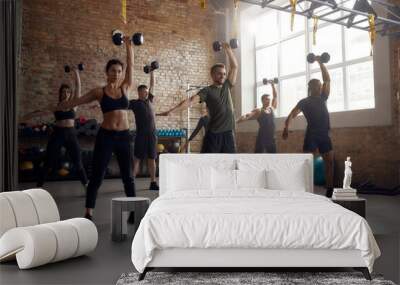 We can do hard things. Full length shot of group of sportive people lifting dumbbell while having workout at industrial gym. Group training, teamwork concept Wall mural