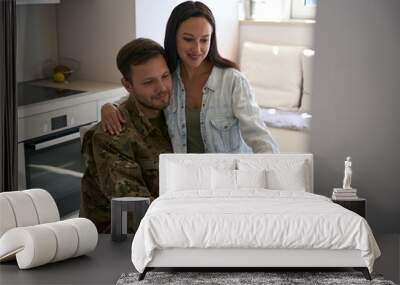 Wife sitting on soldier lap while using laptop in kitchen Wall mural