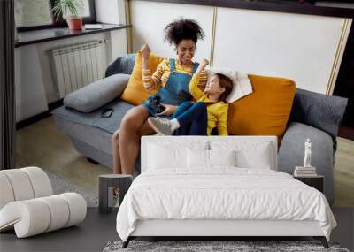 Winners. African american woman, baby sitter and caucasian cute little girl having fun together, playing video games, sitting on the couch. Children education, leisure activities, babysitting concept Wall mural