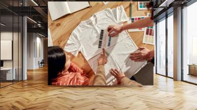 Writing that sells. Creative people trying on stickers with text, while discussing logo and design of T-shirt. Young man and women working together at custom T-shirt, clothing printing company Wall mural