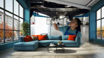 Young afro american girl checking bottom of car on lift Wall mural