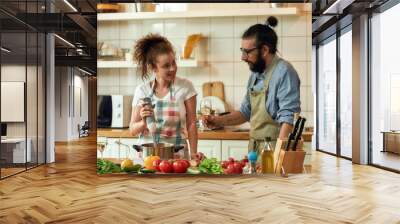 Young couple preparing a meal together in the kitchen. Italian man, chef cook looking at his girlfriend, holding glass of white wine. Cooking at home, Italian cuisine Wall mural