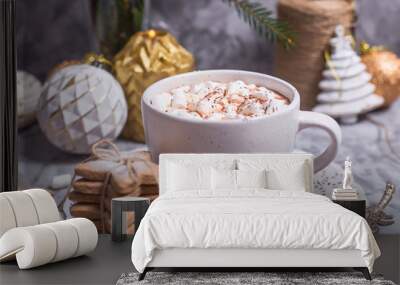 A white cup with hot cocoa with marshmallow stands on a gray table among white and gold Christmas ornaments and fir branches Wall mural