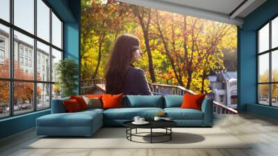 A young beautiful Caucasian girl with dark hair walks around the city and looks at the bright autumn trees in the park. Wall mural