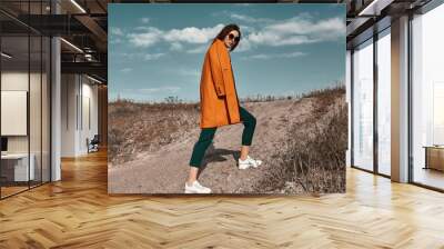 Autumn fashion. Beautiful attracrive young woman in bright autumn look. Orange trendy coat and pants and fashion sunglasses. Wall mural