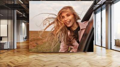 Happy young smilling woman enjoying nature traveling in a car and looking out. Wall mural