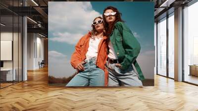 High fashion portrait of two stylish beautiful woman in trendy jackets and jeans posing outdoor. Vogue style. Wall mural