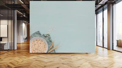 Bowl of dry oat flakes with ears of wheat on light blue background. Cooking oats porridge concept Wall mural