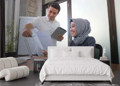 muslim businesswoman and handsome man working together with laptop tablet and paper near windows with white board showing graphic chart Wall mural