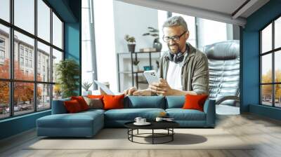 A man is sitting at a desk with a laptop and a cell phone. He is smiling and he is enjoying himself Wall mural