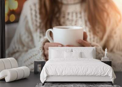 A woman is holding a white mug of coffee in her hands while sitting in front of a fireplace. Concept of warmth and comfort, as the woman enjoys her hot beverage on a chilly day Wall mural