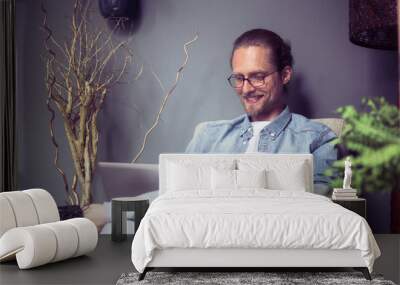 Happy freelancer man sitting at chair, working. Hipster guy smiling while working on laptop. Toned image. Wall mural