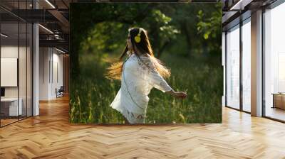 Happy young girl dancing with headphones on. Joyful lady in pretty white dress spins around in field of tall grass dancing to music she hears in her headphones. Wall mural