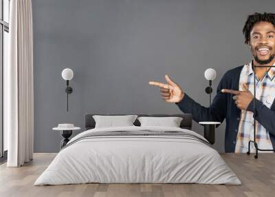 Pointing or directing young african american man in dark navy jumper with both hands turn sideways looking at camera and smile, isolated on grey background. Elegant male model in studio. copy space.  Wall mural