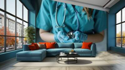 A healthcare professional in teal scrubs holds a stethoscope, ready to provide quality medical care and support to patients. Wall mural