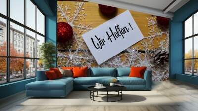 Wir Helfen write on white paper with wooden backgroud. It means We Help. Frame of Christmas Decoration. Wall mural