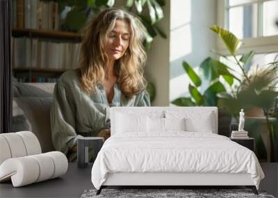 Happy mature woman reading book while resting on comfortable in bright living room. Wall mural