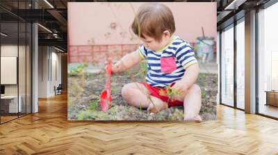 A boy plays with a spatula on the street. Baby boy and red shovel. Boy 0-1 years old Wall mural