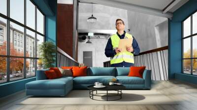 architecture, construction business and building concept - male supervisor in safety west with clipboard working at office Wall mural