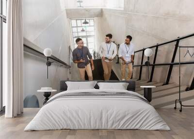 business, people and corporate concept - group of men with conference badges, folder, tablet pc computer and smartphone walking up office stairs Wall mural