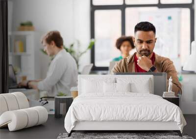 business and creative people concept - young indian man with laptop computer working at office Wall mural