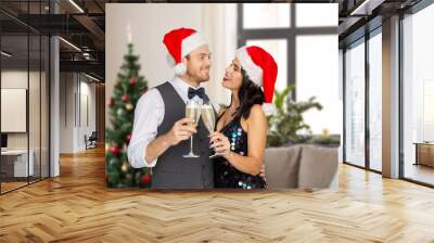 celebration, people and holidays concept - happy couple in santa hats with glasses of non alcoholic champagne over christmas tree on home background Wall mural