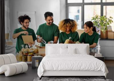 charity, donation and volunteering concept - international group of happy smiling volunteers packing food in boxes according to list on clipboard at distribution or refugee assistance center Wall mural