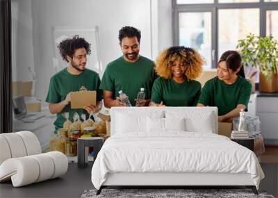 charity, donation and volunteering concept - international group of happy smiling volunteers packing food in boxes according to list on clipboard at distribution or refugee assistance center Wall mural