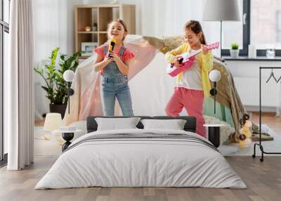 childhood, hygge and friendship concept - happy girls with guitar and microphone playing music and singing near kids tent or teepee at home Wall mural