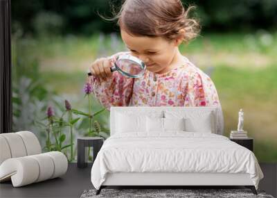 childhood, leisure and people concept - happy little baby girl with magnifier looking at flowers in summer garden Wall mural