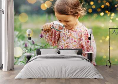 childhood, leisure and people concept - happy little baby girl with magnifier looking at flowers in summer garden Wall mural