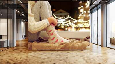 childhood, sadness and people concept - close up of girl in sweater sitting on sill at home window over christmas lights background Wall mural