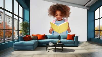 childhood, school and education concept - happy little african american girl with backpack reading book over grey background Wall mural