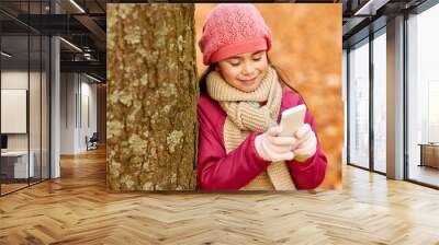 childhood, season and people concept - happy girl with smartphone at autumn park Wall mural