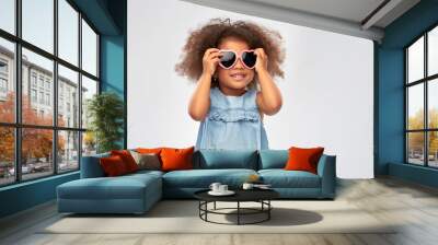 childhood, summer accessory and valentines day concept - happy little african american girl in heart shaped sunglasses over grey background Wall mural