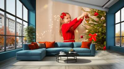 christmas, holidays and childhood concept - happy girl in red dress decorating natural fir tree Wall mural