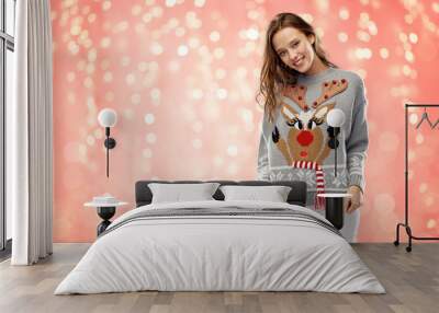 christmas, people and holidays concept - happy young woman wearing ugly sweater with reindeer pattern over festive lights on pink coral background Wall mural