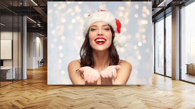 christmas and holidays concept - happy smiling young woman with empty hands in santa hat over festive lights background Wall mural