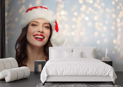 christmas and holidays concept - happy smiling young woman with red lipstick in santa hat over festive lights background Wall mural