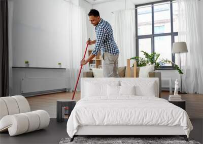 cleaning, housework and housekeeping concept - indian man with broom sweeping floor at home Wall mural